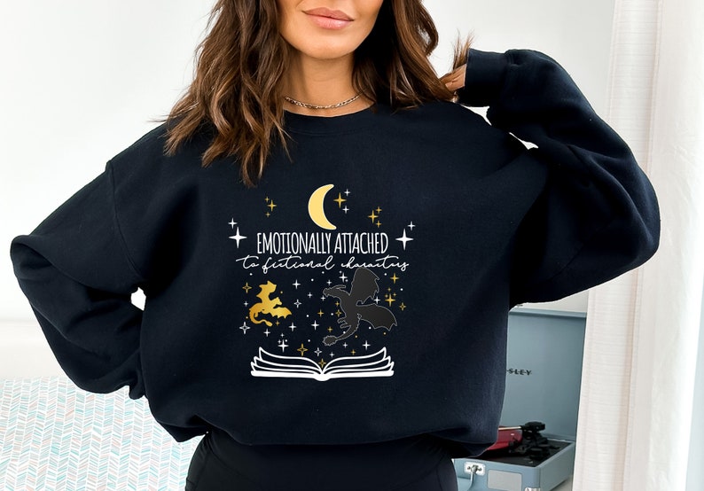 May include: Black sweatshirt with a white graphic design that says "Emotionally attached to fictional characters". The graphic also includes a crescent moon, stars, and two dragons.