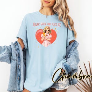 May include: Pale blue t-shirt with the text "SUGAR, SPICE AND FUCK ICE" in red. The shirt features a graphic of a vintage-style illustration of a woman holding an ice cream bar inside a red heart. The word "Chambray" is written in cursive.