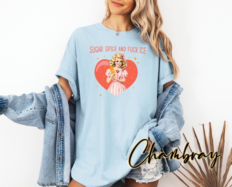 May include: Pale blue t-shirt with the text "SUGAR, SPICE AND FUCK ICE" in red. The shirt features a graphic of a vintage-style illustration of a woman holding an ice cream bar inside a red heart. The word "Chambray" is written in cursive.