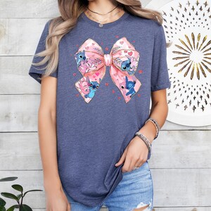 Peut inclure: Un t-shirt bleu marine avec un n&oelig;ud rose orn&eacute; de plusieurs personnages de dessin anim&eacute; Stitch. Le n&oelig;ud a un contour dor&eacute; et est entour&eacute; de petits c&oelig;urs roses.