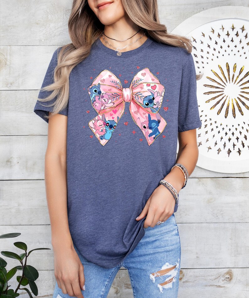 Peut inclure: Un t-shirt bleu marine avec un n&oelig;ud rose orn&eacute; de plusieurs personnages de dessin anim&eacute; Stitch. Le n&oelig;ud a un contour dor&eacute; et est entour&eacute; de petits c&oelig;urs roses.