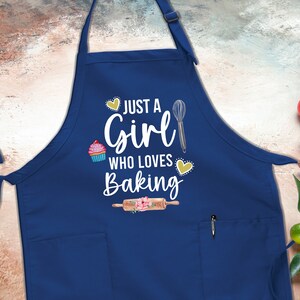May include: A blue apron with a white pocket and the text "Just a Girl Who Loves Baking" in white with a cupcake, whisk, and rolling pin graphic.