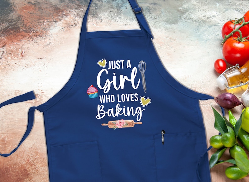 May include: A blue apron with a white pocket and the text "Just a Girl Who Loves Baking" in white with a cupcake, whisk, and rolling pin graphic.