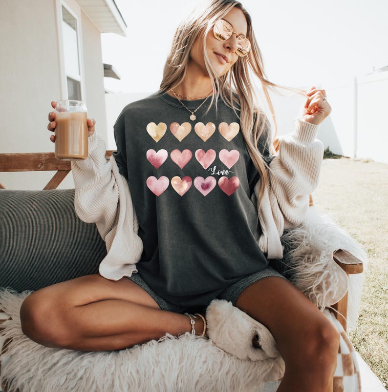 Puede incluir: Una camiseta gris antracita con un dise&ntilde;o de acuarela de corazones rosas y dorados. La camiseta tiene la palabra "Love" escrita en blanco en la parte delantera.