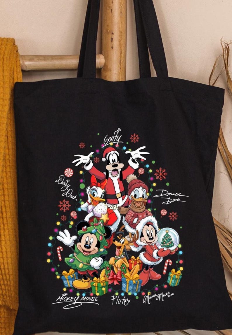 May include: Black tote bag featuring a festive Christmas design with Disney characters. Goofy, Daisy Duck, Donald Duck, Mickey Mouse, Pluto, and Minnie Mouse are dressed in holiday attire. The bag includes the characters' signatures and colorful Christmas lights.