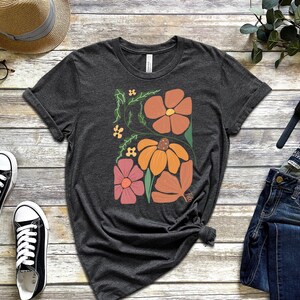 May include: A dark grey t-shirt with a floral design featuring orange, pink, and yellow flowers on a dark grey background.