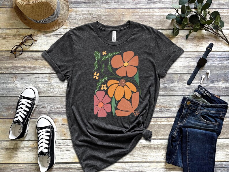 May include: A dark grey t-shirt with a floral design featuring orange, pink, and yellow flowers on a dark grey background.