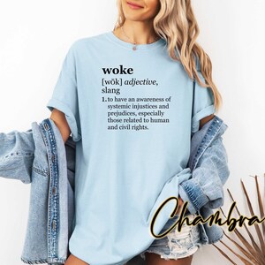 May include: A light blue t-shirt with the word "woke" defined as "to have an awareness of systemic injustices and prejudices, especially those related to human and civil rights."