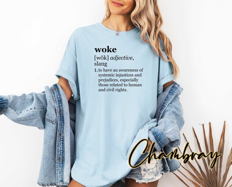 May include: A light blue t-shirt with the word "woke" defined as "to have an awareness of systemic injustices and prejudices, especially those related to human and civil rights."