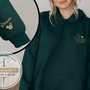 May include: Dark green hoodie with gold embroidered Mickey Mouse and text. The left sleeve features the word "Dream" and a Mickey Mouse head. The hoodie is a personalized gift, embroidered with the words "Sweatshirt & Hoodie".