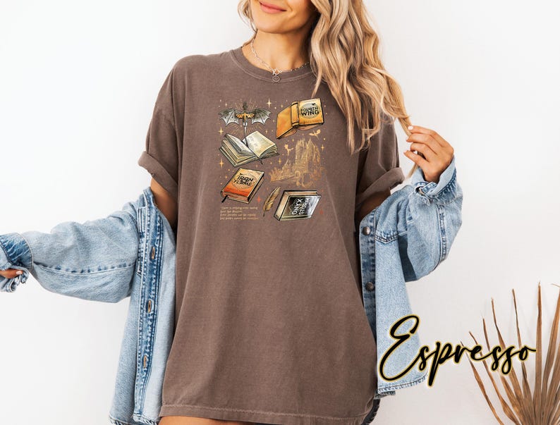 May include: Espresso-coloured t-shirt with a graphic of open books, a bat, and a castle. The text on the shirt includes the words "Iron Flame" and other text. The shirt is worn with a blue denim jacket.