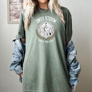 May include: A green oversized t-shirt with a graphic print of a dragon and the text "ONYX STORM" and "BRAVE THE DARK".