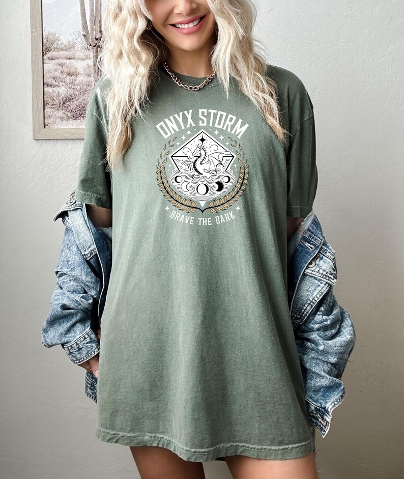 May include: A green oversized t-shirt with a graphic print of a dragon and the text "ONYX STORM" and "BRAVE THE DARK".