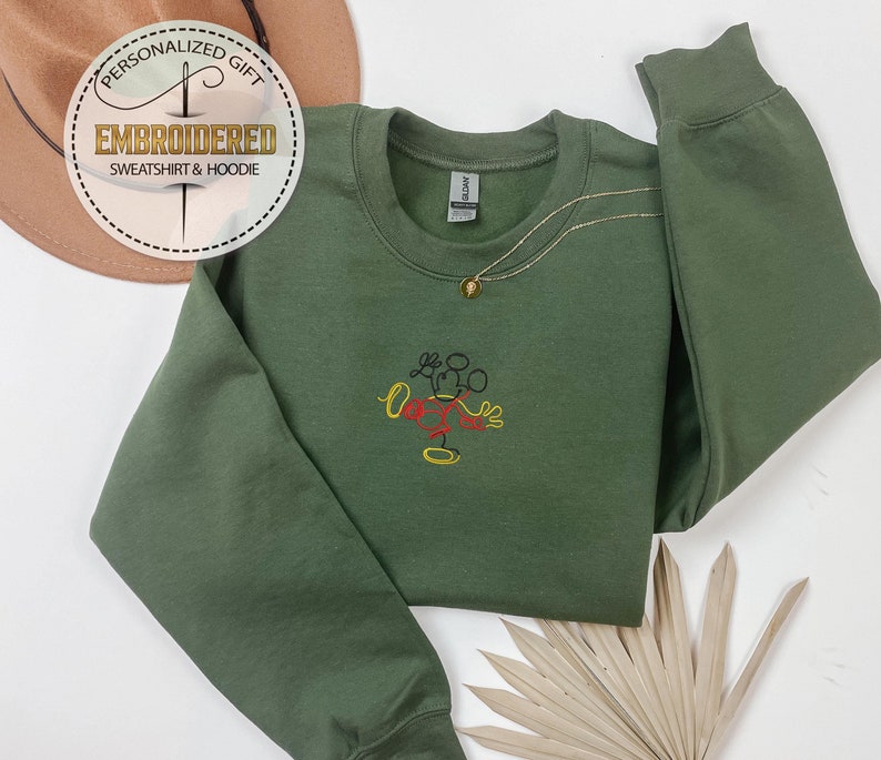 May include: A green sweatshirt with a black, red, and yellow embroidered Mickey Mouse design. The sweatshirt has a crew neck and long sleeves.