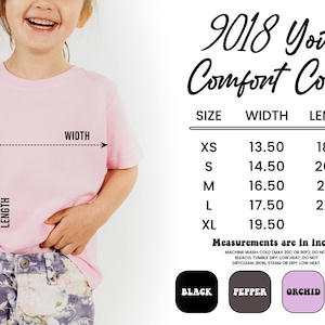 May include: A child wearing a pale pink t-shirt. The image includes a size chart with measurements in inches. Sizes range from XS to XL, with width and length dimensions. Available colours are black, pepper, orchid, and blossom.