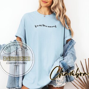 May include: Light blue t-shirt with the text "in my Disney mom era" in black script. The shirt has a relaxed fit and is part of a personalized gift collection. The shirt is made of Comfort Colors material.