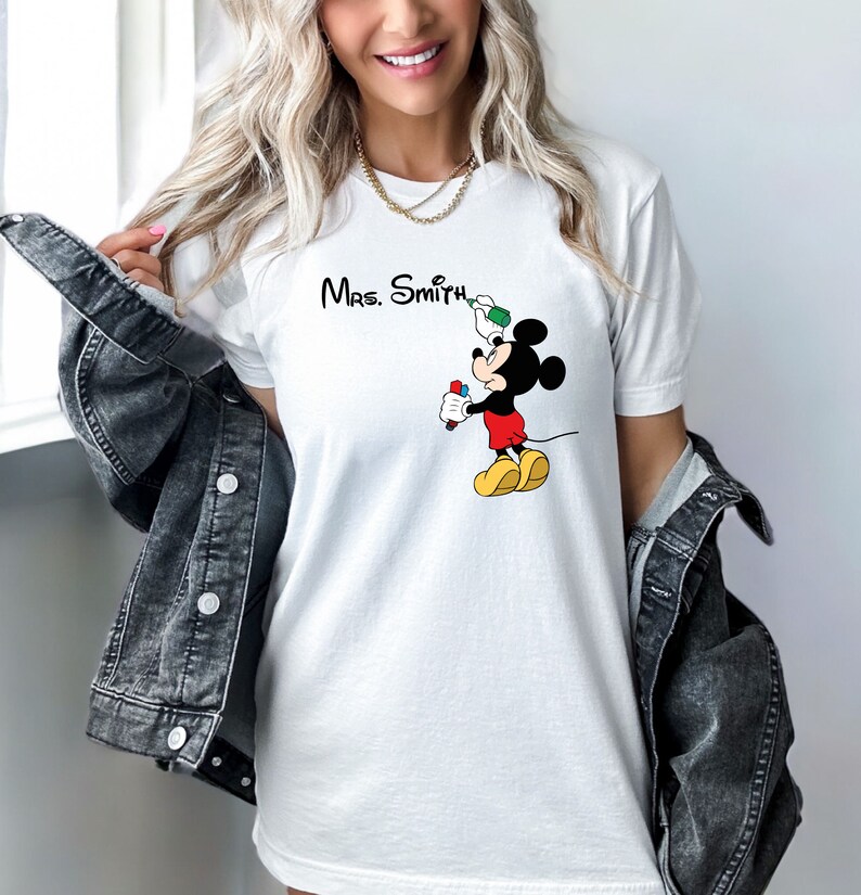 May include: White t-shirt with a Mickey Mouse graphic holding a marker and a paintbrush. The text "Mrs. Smith" is printed above Mickey Mouse.
