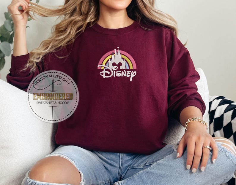 May include: A maroon sweatshirt with a rainbow and castle graphic and the text "Disney" in white.