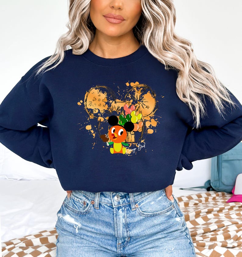 May include: Navy blue sweatshirt featuring a cartoon character with a Mickey Mouse-inspired head, holding balloons. The design includes a gold-colored Mickey Mouse head outline with paint splatters. The sweatshirt is a comfortable, casual style.