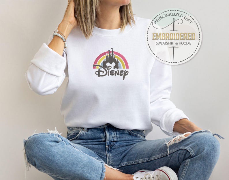 May include: White sweatshirt with a rainbow and the Disney castle with the word "Disney" underneath. The sweatshirt is being worn by a person.