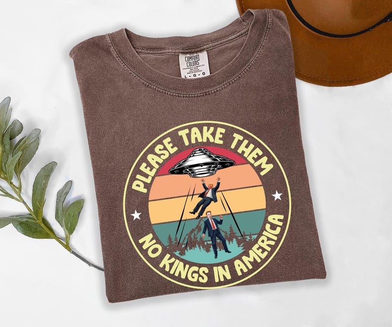 Op de afbeelding: Bruin Comfort Colors T-shirt met een cirkelvormige afbeelding met een retro zonsondergang, een UFO en twee figuren die worden ontvoerd. De tekst luidt "PLEASE TAKE THEM" en "NO KINGS IN AMERICA".