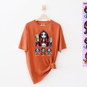 May include: Orange t-shirt with a graphic of a woman with red hair and a black and white striped dress holding a coffee cup. The woman is surrounded by three smaller figures with the names "Emilia", "Luke", and "Nora" written below them. The text "MAMA" is written on the woman's dress.