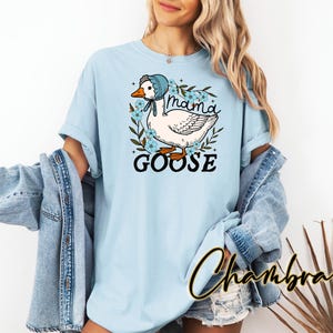 Puede incluir: Camiseta azul claro con un gr&aacute;fico de un ganso con un gorro azul y el texto "Mama Goose".