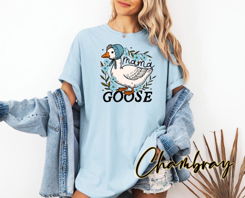 Puede incluir: Camiseta azul claro con un gr&aacute;fico de un ganso con un gorro azul y el texto "Mama Goose".