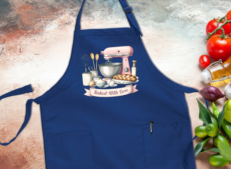 May include: Blue kitchen apron with a pocket and a white graphic of a pink stand mixer, ingredients, and bread with the text "Baked With Love".