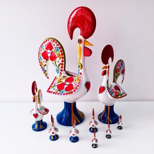 Puede incluir: Un conjunto de siete figuras de gallo coloridas, cada una con un diseño único. El gallo más grande es blanco con detalles rojos, rosas y azules. Los gallos más pequeños son blancos con detalles rojos, azules y amarillos. Los gallos están hechos de cerámica y están pintados a mano.