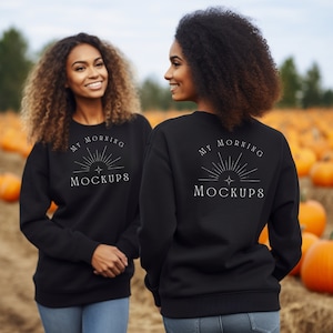 May include: Two people wearing black sweatshirts with the text "MY MORNING MOCKUPS" in white. The sweatshirts are plain and have a crew neck design. The background is a pumpkin patch with pumpkins.