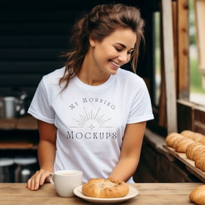 May include: A woman wearing a white t-shirt with the text "My Morning Mockups" and a sun graphic. She is sitting at a table with a cup of coffee and a pastry.
