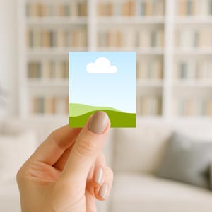 Könnte beinhalten: Eine kleine, quadratische Karte mit einer Landschaftsillustration. Das Design umfasst einen blauen Himmel mit einer weißen Wolke, grüne Hügel und einen hellblauen Hintergrund. Die Karte wird von einer Hand mit neutralem Nagellack gehalten.