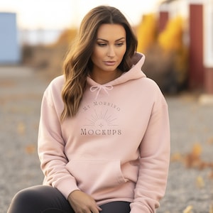 Puede incluir: Una sudadera con capucha rosa claro con capucha con cordón y bolsillo delantero. El texto "MY MORNING MOCKUPS" está impreso en la parte delantera. La sudadera está hecha de un material suave.