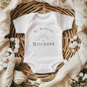 Puede incluir: Un body blanco para bebé con mangas cortas y un diseño gráfico negro que dice "My Morning Mockups" con un gráfico de sol estilizado.