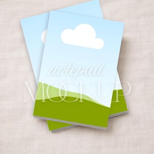 May include: Two notepads with a sky blue background and a white cloud graphic. The bottom of the notepad features a green landscape design. The word "notepad" is written in a light font across the image.