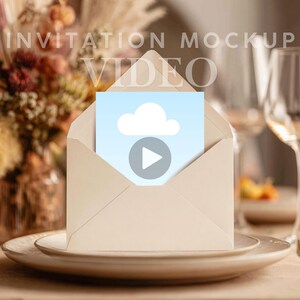 Puede incluir: Un sobre beige con una tarjeta azul claro con una nube blanca y un icono de reproducción. El sobre está sobre un plato blanco, con un fondo borroso de flores y cristalería. El texto de la imagen dice "INVITATION MOCKUP VIDEO."