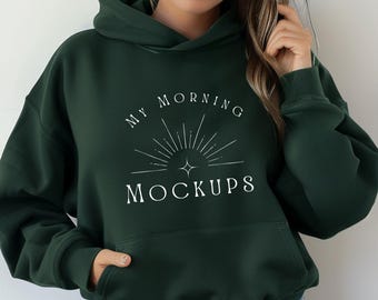 May include: A dark forest green hooded sweatshirt featuring a white graphic print on the chest. The design includes a stylized sunburst icon above the text "MY MORNING MOCKUPS" in a clean, serif font. The hoodie has long sleeves and a front pocket.