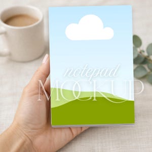 Könnte beinhalten: Ein rechteckiger Notizblock mit einer Grafik aus einer weißen Wolke vor einem hellblauen Himmel über grünen Hügeln. Der Text "notepad MOCKUP" ist in Weiß in der Mitte des Designs aufgedruckt, das vor einem neutralen Hintergrund gehalten wird.