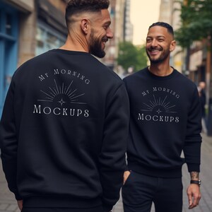 May include: Two people wearing black sweatshirts with the text "My Morning Mockups" on the back. The sweatshirts feature a sunburst design with a star in the centre.