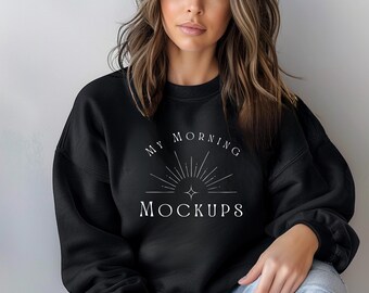 May include: A black long-sleeve crewneck sweatshirt featuring white text that reads MY MORNING MOCKUPS above a graphic of a sunburst with a central four-pointed star. The sweatshirt has a ribbed collar, cuffs, and hem, and is worn with blue jeans.