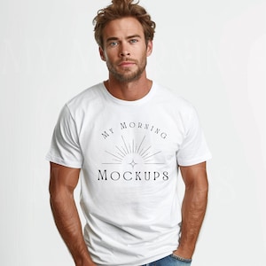 Op de afbeelding: Een wit T-shirt met ronde hals en de tekst "MY MORNING MOCKUPS" in zwart. Het ontwerp heeft een sunburst-afbeelding. De persoon draagt een blauwe spijkerbroek.