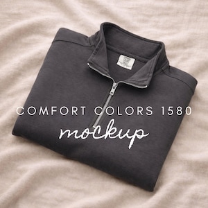 May include: A dark charcoal gray quarter-zip pullover sweatshirt featuring a silver metal zipper and a stand-up collar. The inner neck label displays the text Comfort Colors 1580. The text COMFORT COLORS 1580 mockup is overlaid on the garment.