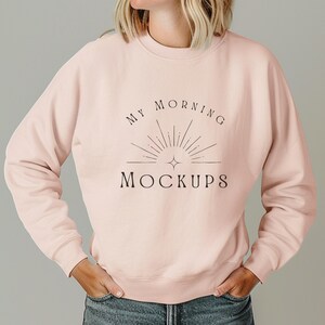 May include: A light pink sweatshirt with the text "MY MORNING MOCKUPS" in black. The design includes a sunburst graphic. The sweatshirt is long-sleeved and has a crew neck.