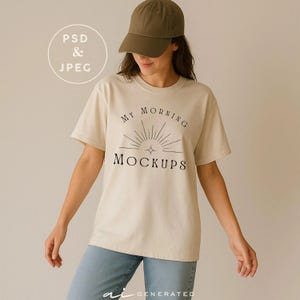 May include: A beige t-shirt featuring a black graphic with a sunburst design and the text "MY MORNING MOCKUPS" in a serif font. The shirt is paired with a solid olive green baseball cap and blue denim jeans, creating a casual ensemble.
