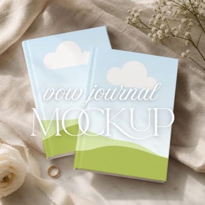 May include: Two light blue vow journals with a cloud and landscape design. The journals have the words "vow journal MOCKUP" printed on the cover. A gold ring and white flowers are in the background.