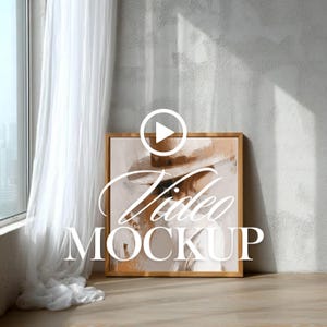May include: A framed artwork with a neutral color palette, featuring a person wearing a hat. The artwork is leaning against a gray wall, with a sheer white curtain and a window visible on the left. The words "Video MOCKUP" are overlaid on the artwork.