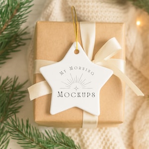 May include: A wrapped gift box with a white star-shaped ornament. The ornament has the text "MY MORNING MOCKUPS" and a sunburst design. The gift is tied with a cream-colored ribbon.