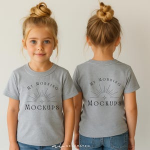 Può includere: Una t-shirt a maniche corte grigio melange con una stampa grafica nera sul petto. Il design include un'icona a raggiera stilizzata sopra il testo "MY MORNING MOCKUPS" in un carattere serif. La maglietta è mostrata sia frontalmente che sul retro.
