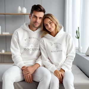 May include: Two people wearing white hooded sweatshirts with the text "My Morning Mockups" printed on the front. The couple is sitting on a white couch.